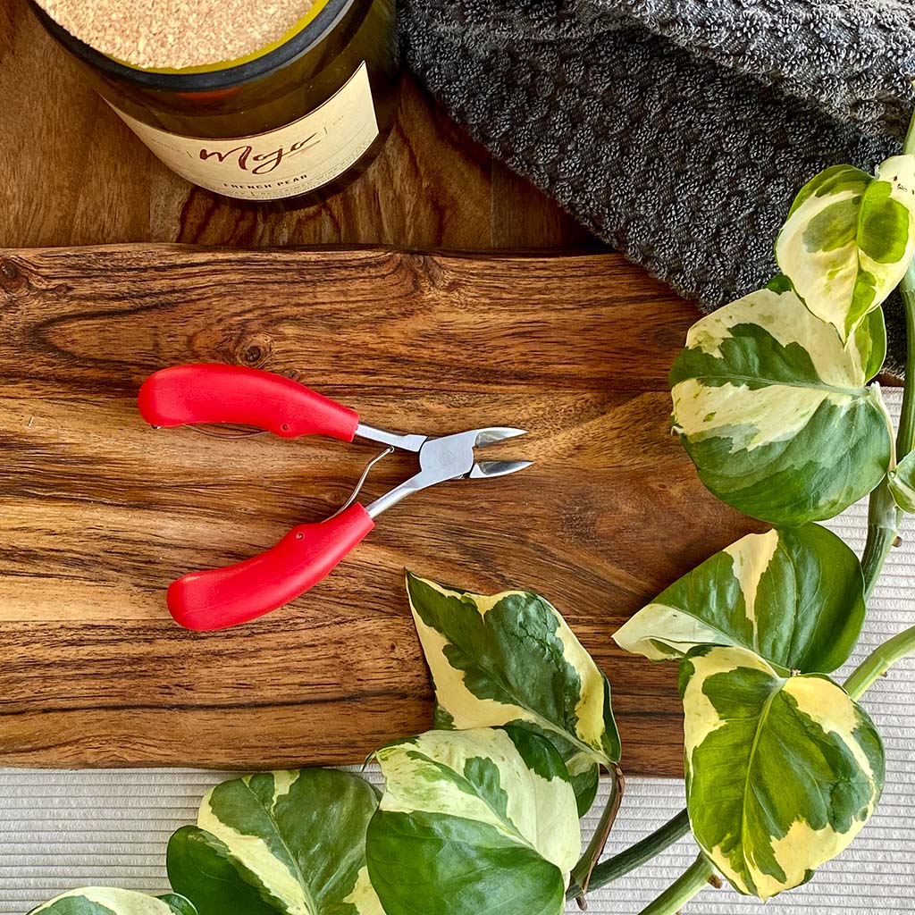 red thick handled nail clippers on wooden board next to candle