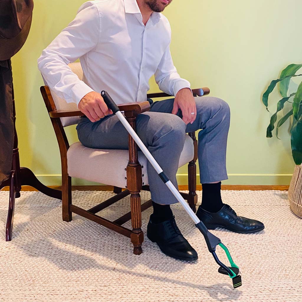 person sitting on vintage chair using reacher grabber to pick up keys
